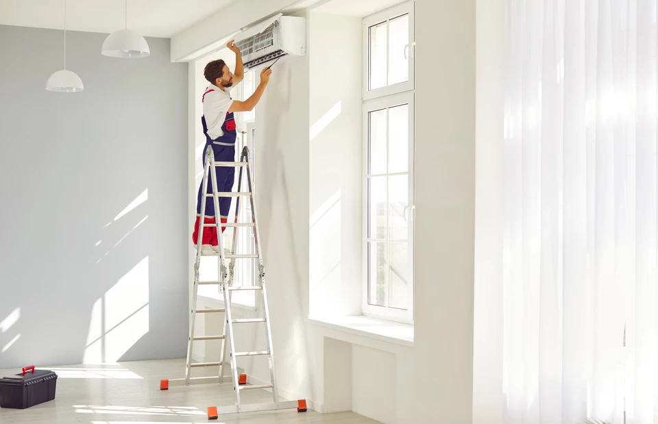 Technicien en combinaison de travail installant une unité de climatisation murale dans un intérieur résidentiel moderne
