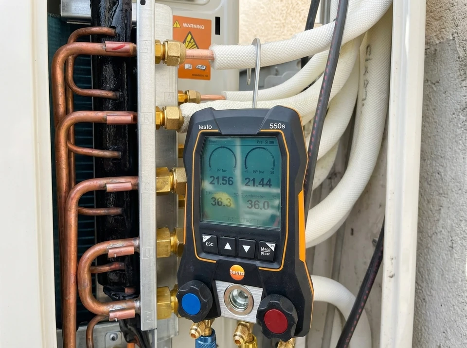 Deux techniciens en bleu travaillent sur une unité extérieure de climatisation